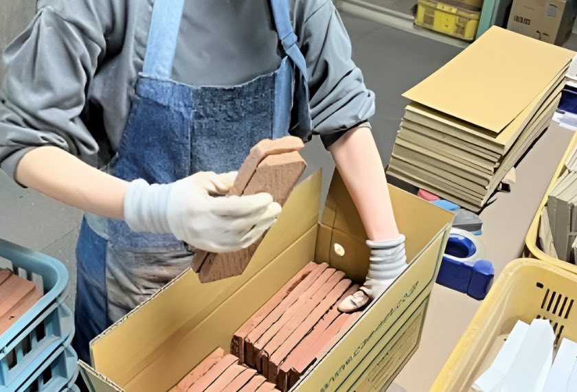 手袋をした手で、焼き上がったレンガ調タイルを箱に詰めているところ